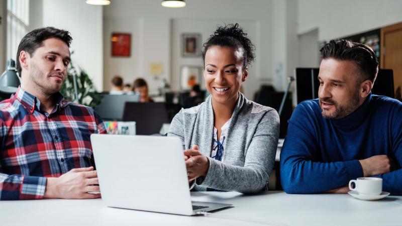 three people gather around a laptop